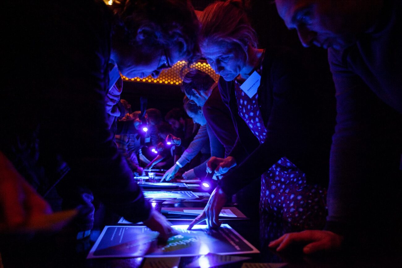 A group of learners in a dark space using ultra violet light to decipher a message.