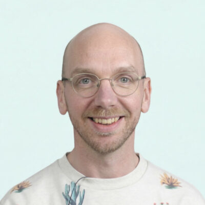 Portrait of Bjorn de Wildt, a white man with a short beard and bald head who wears glasses and is smiling.