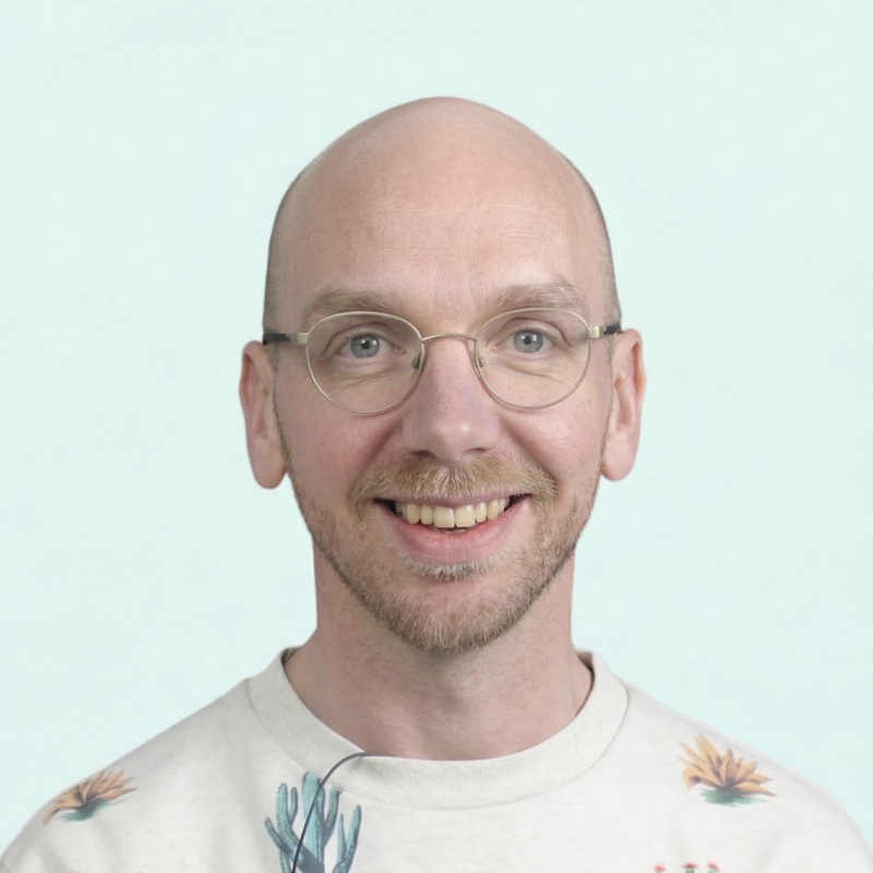Portrait of Bjorn de Wildt, a white man with a short beard and bald head who wears glasses and is smiling.