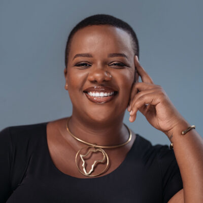 Portrait of Henriette Paula Mugisa, a black woman with short dark hair, who is smiling with her left and to the side of her head.