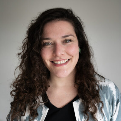 Portrait of Romy Alexandra, a young white woman with long dark curly hair.