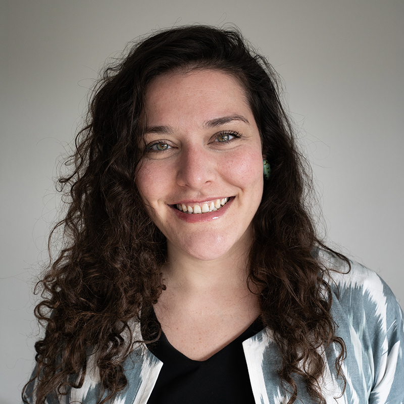 Portrait of Romy Alexandra, a young white woman with long dark curly hair.